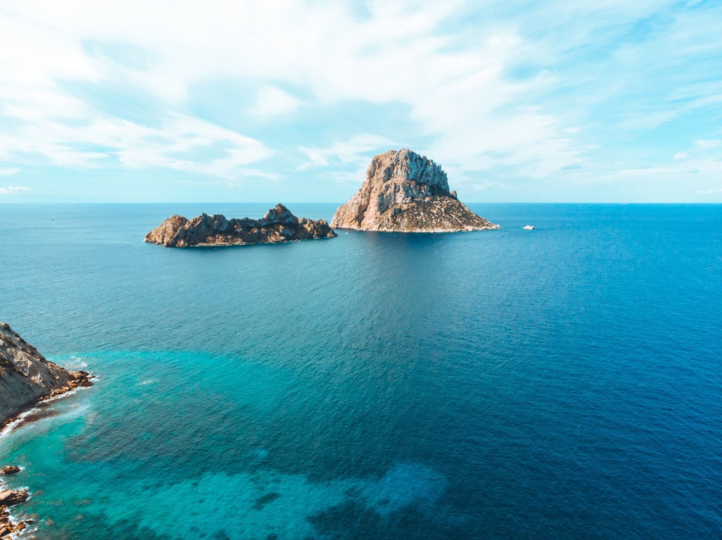 Aerial view of Ibiza's pristine coastline with white sandy beaches, turquoise Mediterranean waters, and luxury yachts anchored in coves