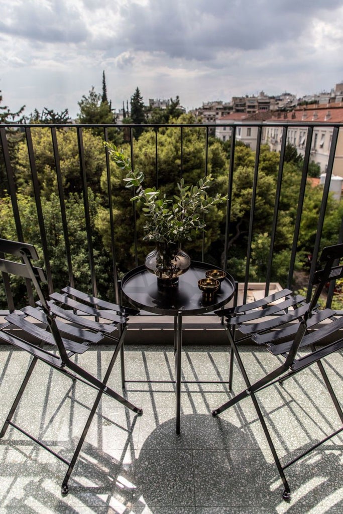 Sleek minimalist hotel room with white marble walls, modern designer furniture, and panoramic view of Athens' cityscape at sunset