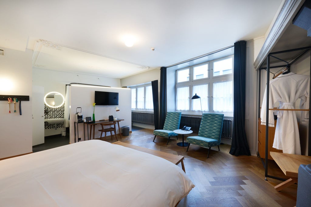 Elegant historic Swiss hotel room with wood-paneled walls, plush king bed, antique furnishings, and large windows overlooking a charming European street scene