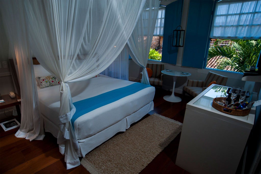 Luxurious turquoise-themed hotel suite with elegant white furniture, polished hardwood floors, and expansive Brazilian coastal view from private balcony