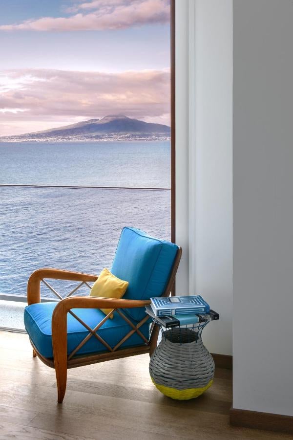 Elegant Mediterranean hotel balcony with blue and white decor, overlooking the Bay of Naples and Vesuvius against a sunset sky