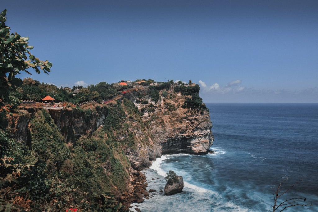 Majestic Uluwatu Temple perched on steep limestone cliffs above crashing waves at sunset, surrounded by lush tropical foliage