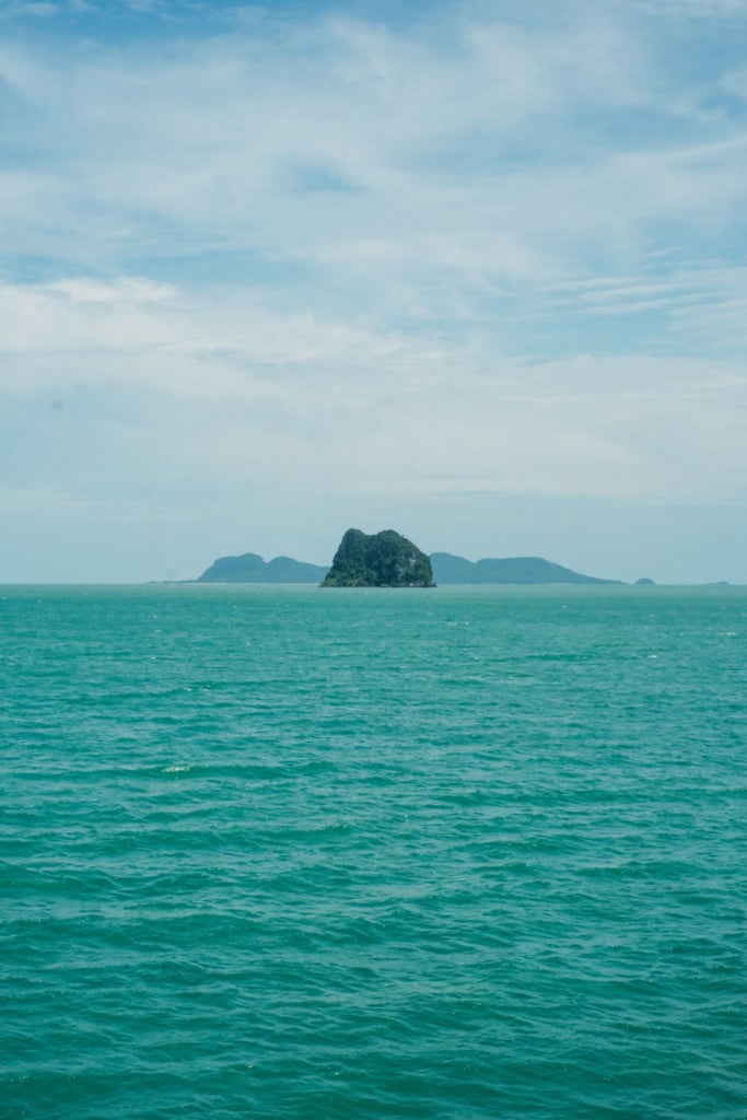 Tranquil private beach at sunset in Koh Samui, with elegant lounge chairs, palm trees, and crystal-clear turquoise waters against an orange sky