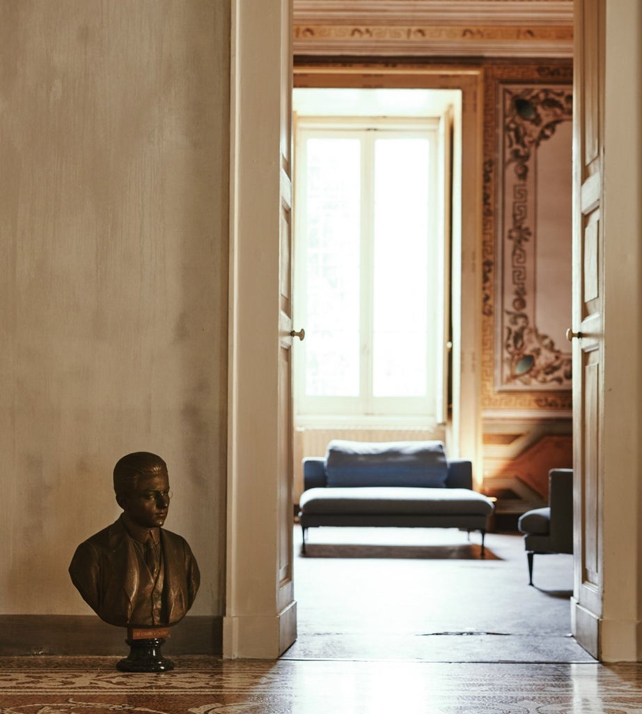 Opulent master suite at Palazzo Daniele, featuring elegant stone floors, high ceilings, minimalist furnishings, and soft natural light streaming through historic windows