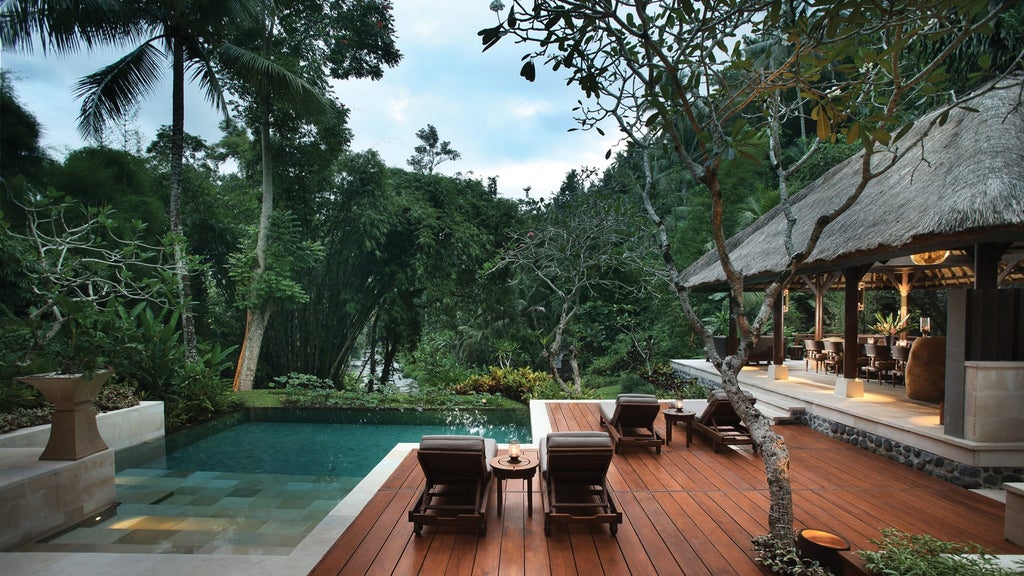 Elegant curved walkway descends to circular lotus pond at Four Seasons Sayan, surrounded by lush tropical Balinese forest at sunset