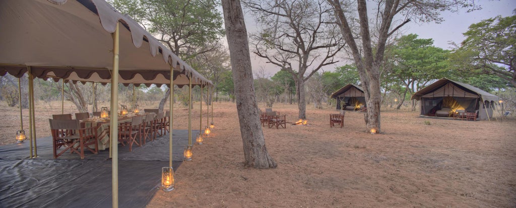 Luxurious safari tent at dusk overlooking Chobe River, with canvas walls, teak furniture and lantern lighting creating a romantic ambiance