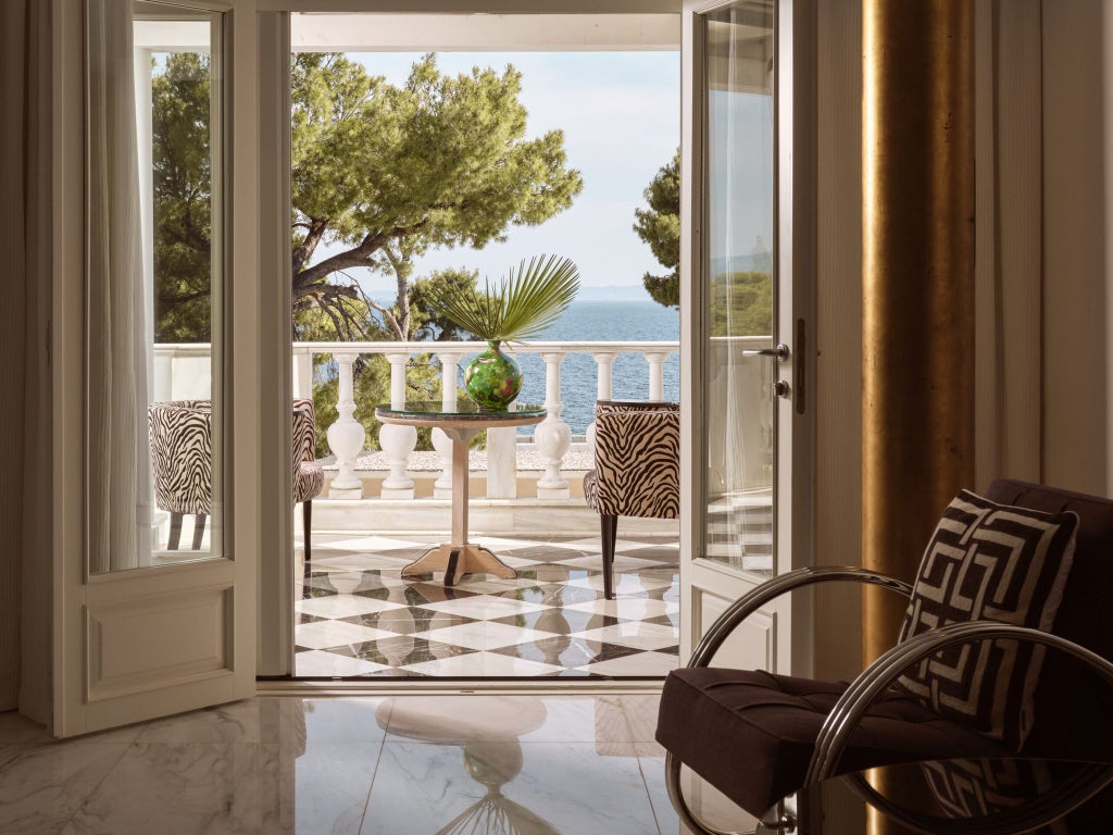 Spacious luxury suite with panoramic Aegean Sea view, elegant white decor, private balcony, and modern design overlooking pristine coastal landscape in Greece