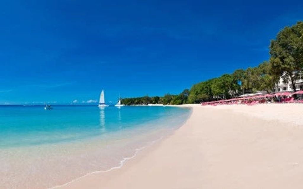 Elegant beachfront resort with coral stone walls, swaying palm trees and turquoise Caribbean waters at sunset in Barbados