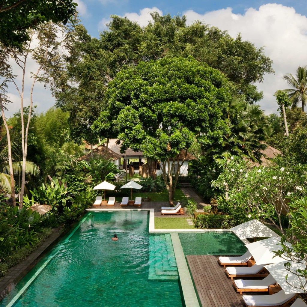 Luxurious infinity pool overlooking lush Balinese jungle valley, with contemporary stone deck and traditional thatched pavilion