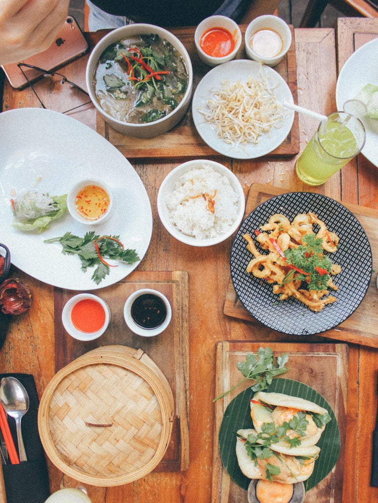 Professional chef demonstrating traditional Indonesian cooking techniques in an elegant Four Seasons kitchen, with vibrant ingredients and gleaming copper cookware