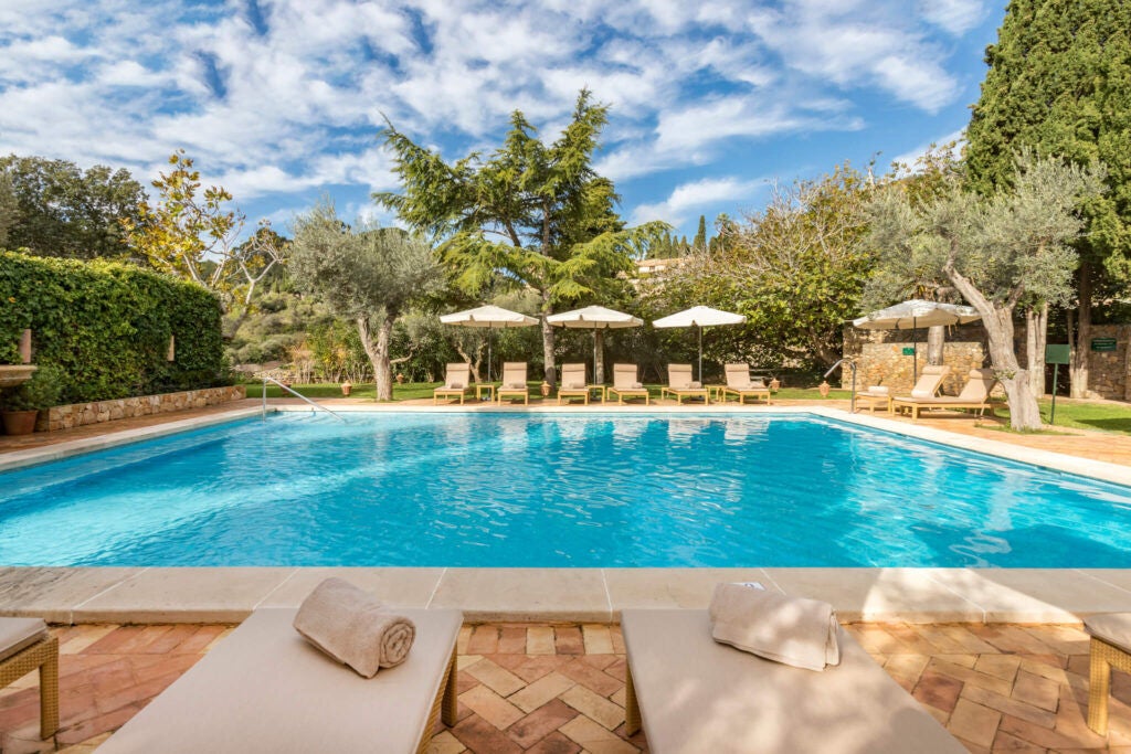 Historic stone hotel with infinity pool overlooking Mallorca's Tramuntana mountains, terracotta roofs, and lush Mediterranean gardens