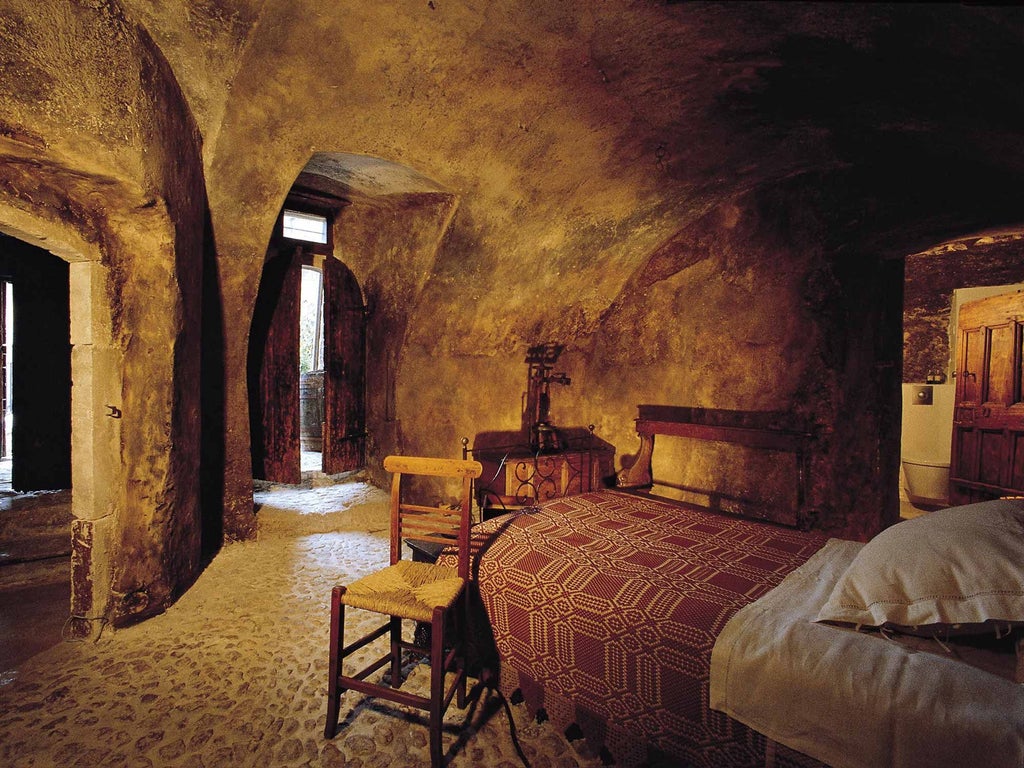 Rustic stone walls, antique wooden furnishings, soft candlelight illuminating a historic Italian hotel room with panoramic mountain village views