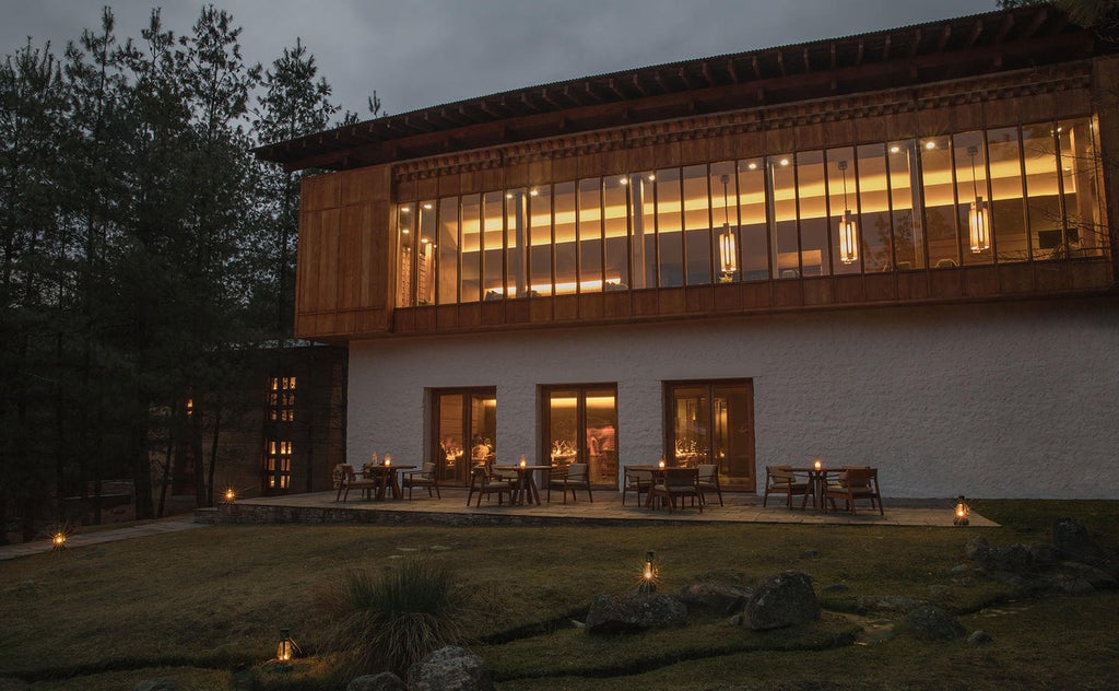 Luxury mountain lodge with traditional Bhutanese architecture nestled in pine forest, featuring stone walls and panoramic valley views