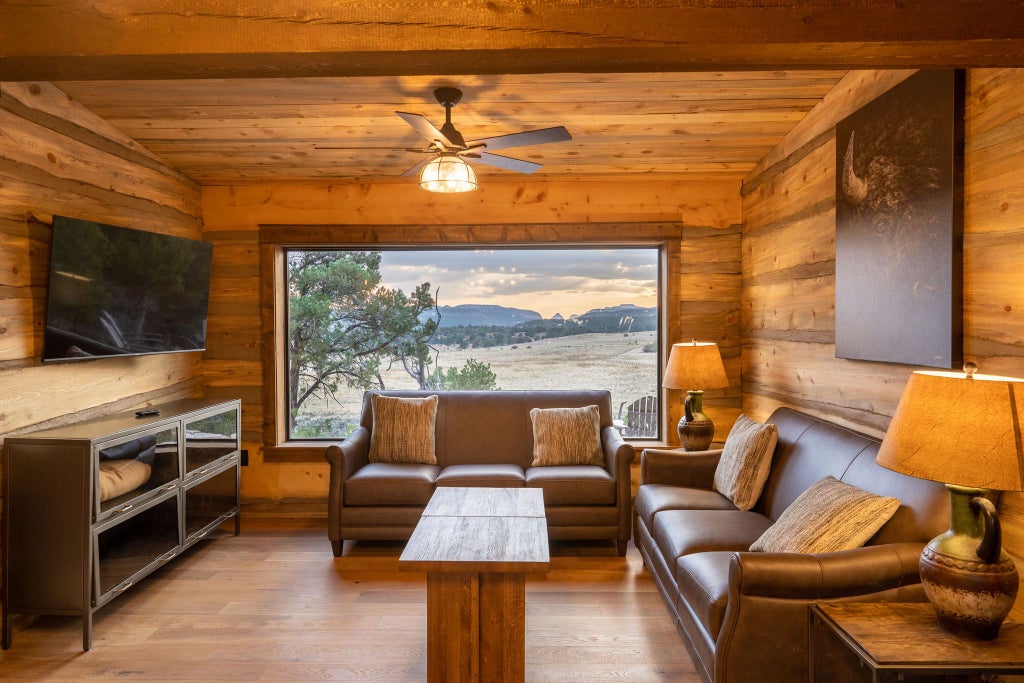 Rustic lodge room with plush bedding, wooden furnishings, and large window overlooking scenic mountain landscape at Scenset Mountain Ranch, United States