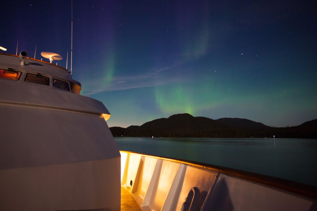 Luxurious dinner cruise ship illuminated at dusk sailing through Norwegian fjords under dramatic northern lights and starlit sky