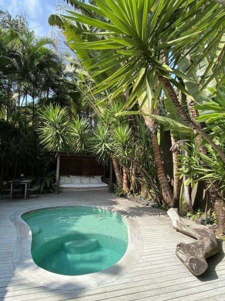 Private oceanfront rustic-luxe villa surrounded by palm trees, with thatched roof, wooden terrace and infinity pool overlooking turquoise sea