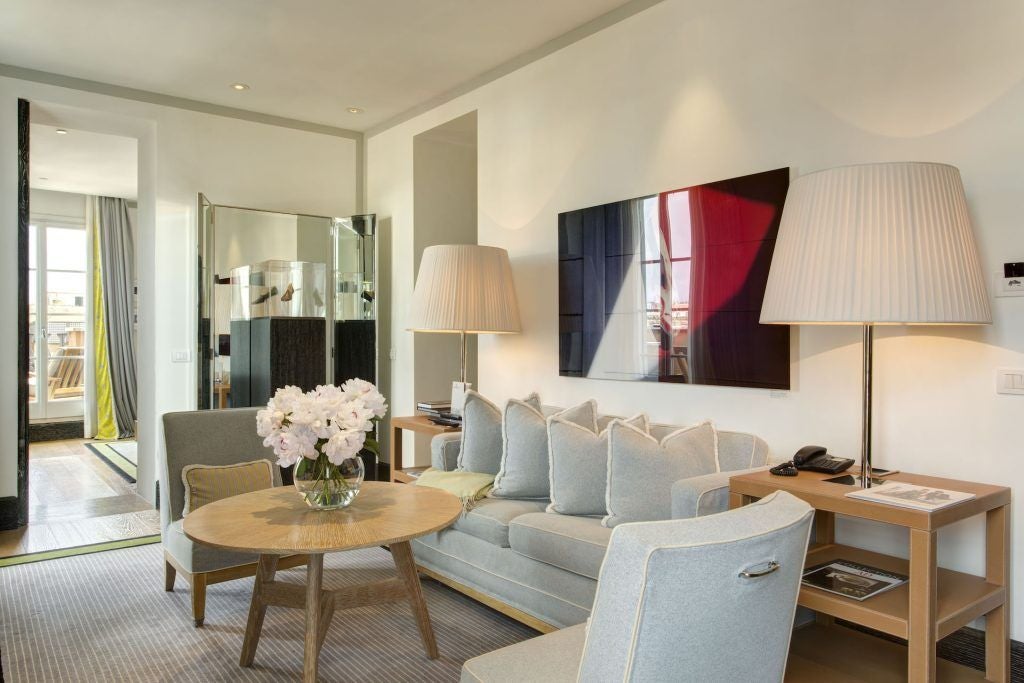 Luxurious penthouse suite overlooking Rome's historic Trinità dei Monti, featuring elegant modern decor, plush furnishings, and panoramic city views at sunset