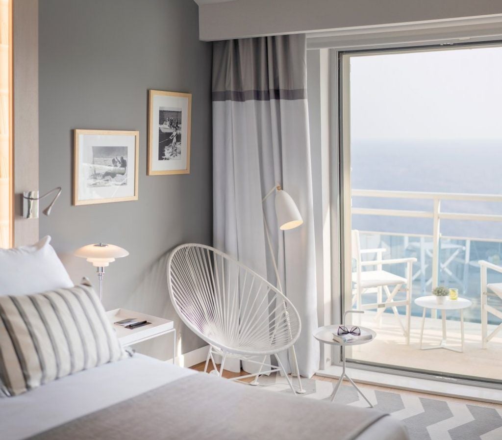 Modern luxury hotel room with panoramic Adriatic Sea views, private balcony, king bed, and contemporary furnishings in muted beige tones