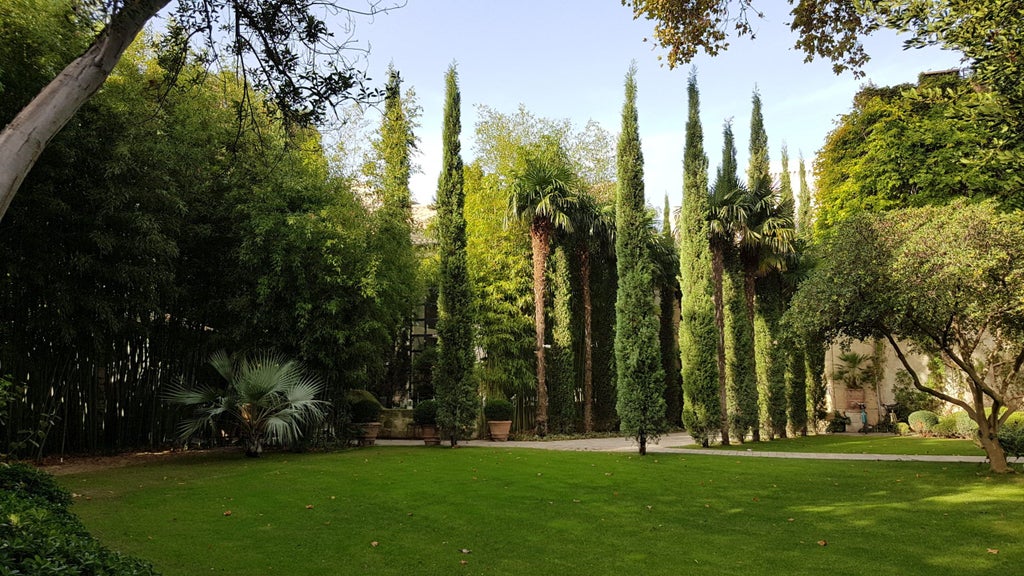 Elegant French hotel courtyard with manicured gardens, marble fountain, and wrought-iron balconies set against limestone walls