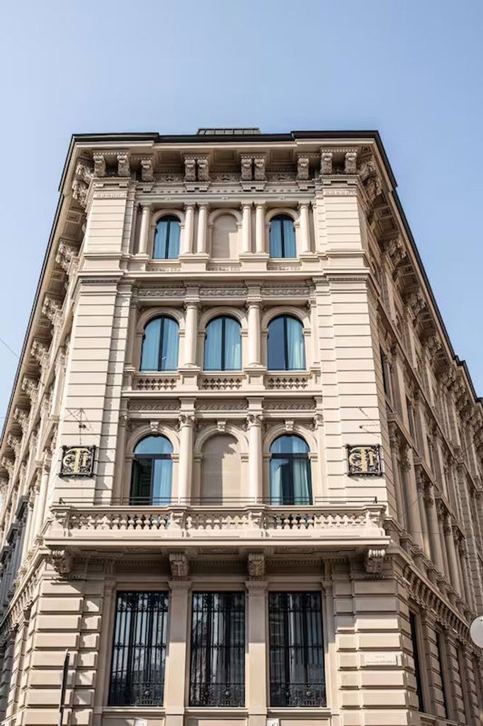 Historic luxury hotel facade with ornate stone architecture, tall arched windows, and decorative columns in Milan's city center