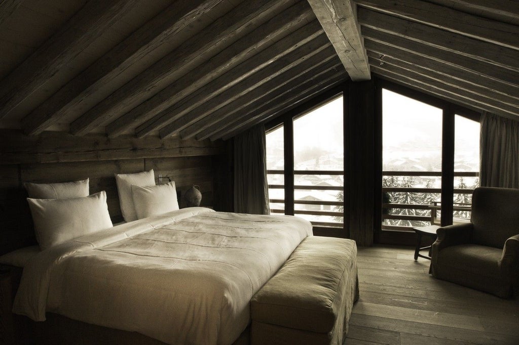 Luxurious alpine suite with wooden walls, plush king bed, large windows overlooking snowy mountain landscape in French ski resort chalet