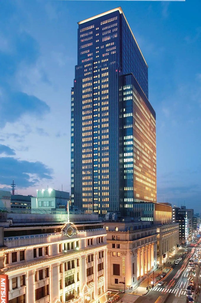 Modern Japanese luxury hotel with illuminated glass facade, rising against Tokyo skyline at dusk, reflecting city lights in its windows