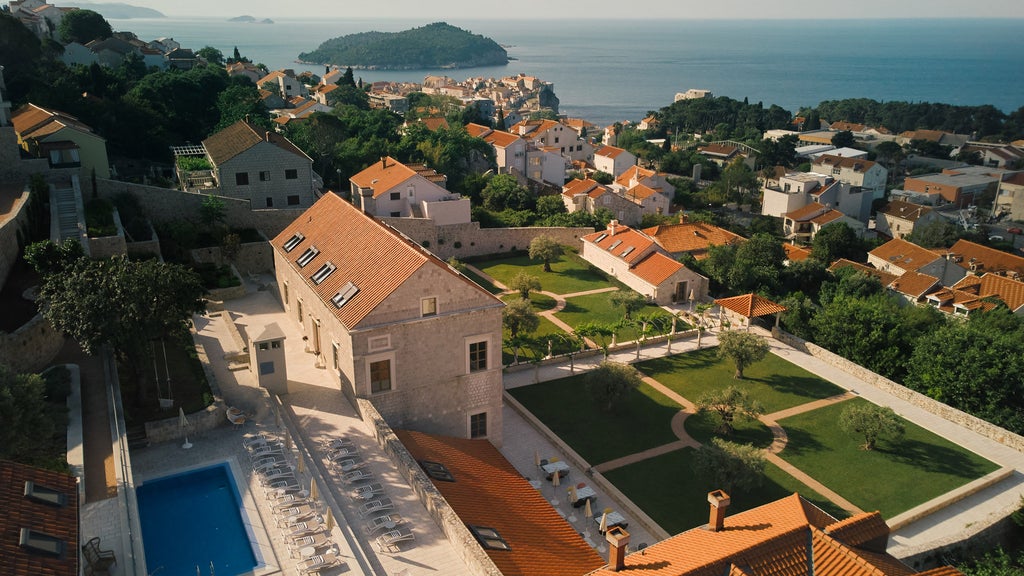 Grand Mediterranean hotel facade with white stone walls, arched windows, ornate balconies and manicured palm trees on a sunny Croatian coast