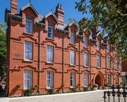 Elegant Victorian-era hotel exterior featuring red brick facade, ornate balconies, and manicured topiaries framing grand entrance steps