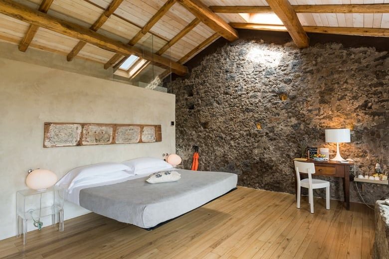 Elegant Sicilian deluxe room with rustic wooden floors, minimalist white linens, and panoramic vineyard views at Monaci delle Terre Nere estate