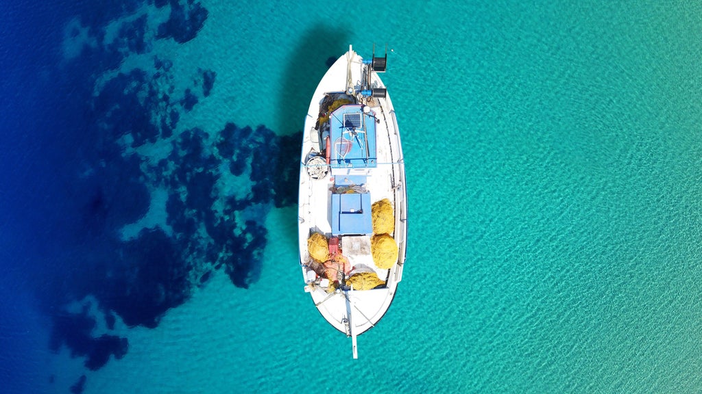 Luxurious sailboat gliding through crystal-clear Aegean waters, passing rocky Greek islands of Koufonissia and Schoinoussa at golden sunset