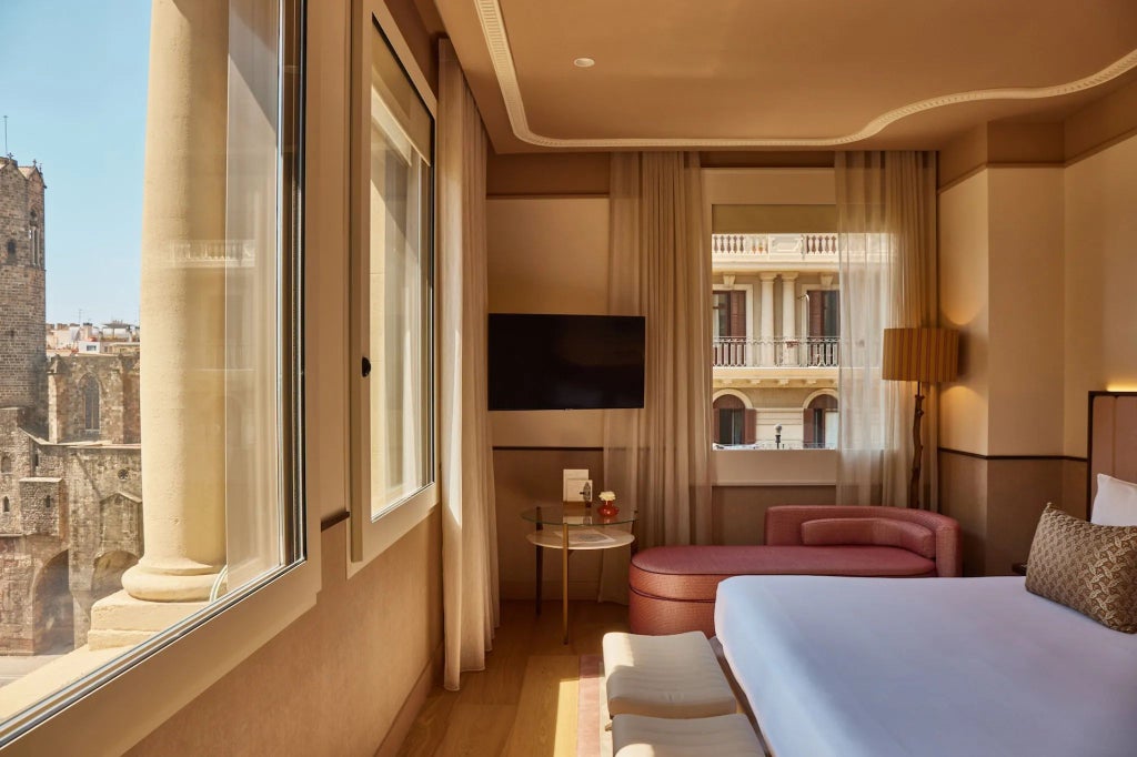 Luxurious deluxe corner hotel room with floor-to-ceiling windows revealing panoramic cityscape of Spanish urban landscape, modern elegant furnishings