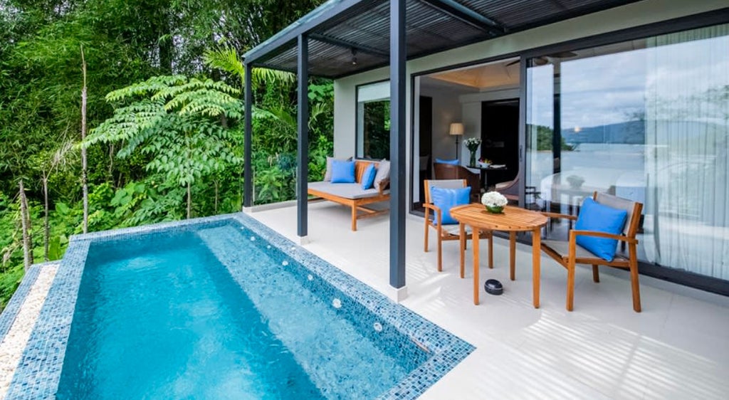 Modern pool suite balcony with private infinity pool overlooking lush tropical gardens, featuring elegant teak loungers and Phuket ocean views.