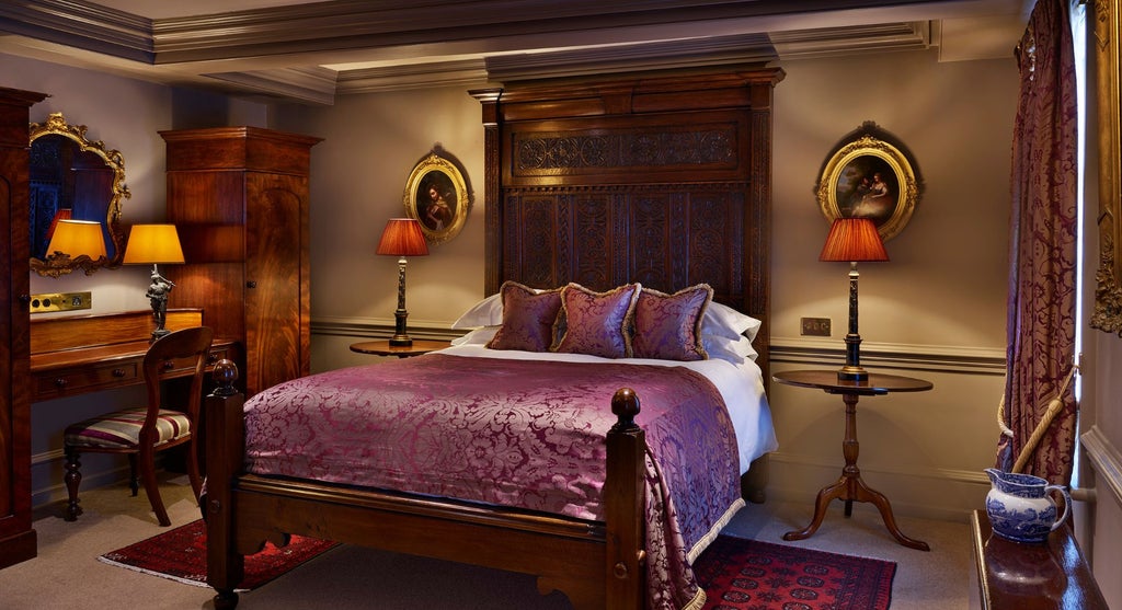 Opulent, warmly-lit deluxe double hotel room with plush burgundy bedding, antique furniture, and elegant period-inspired design in a UK boutique setting