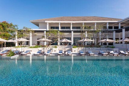 Luxurious beachfront resort with minimalist design, featuring sleek infinity pool overlooking turquoise waters of Vietnam's scenic coastline at sunset