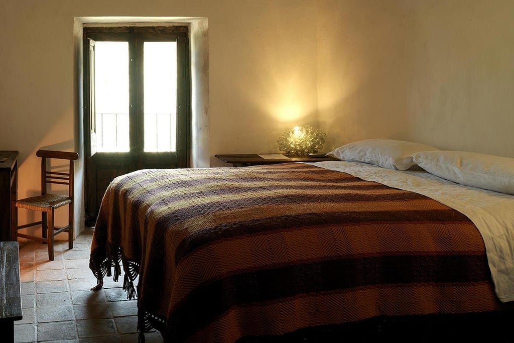 Rustic stone walls, antique wooden furnishings, soft candlelight illuminating a traditional Italian mountain hotel room with handcrafted textiles and warm ambiance