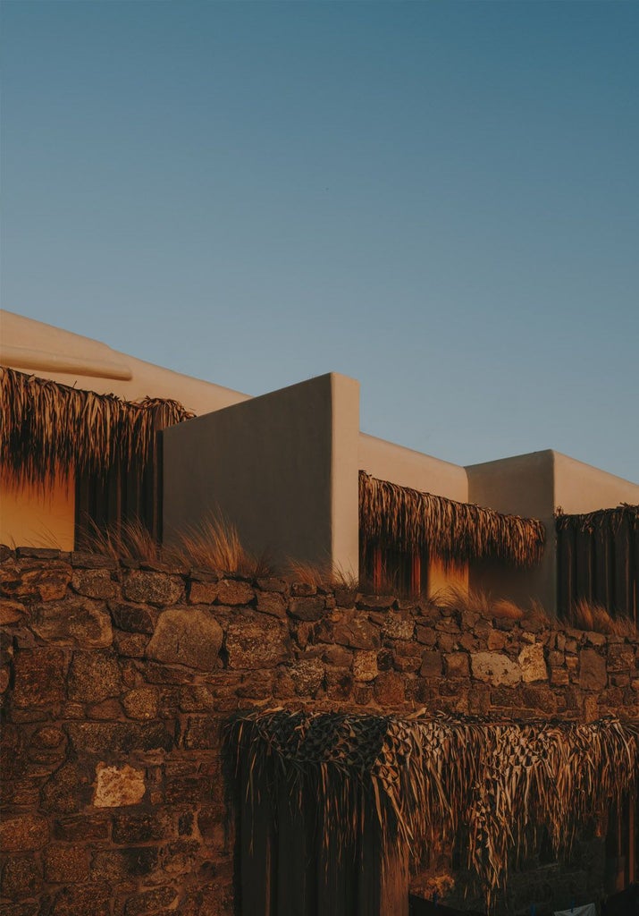 Luxury minimalist hotel overlooking azure Aegean waters, white geometric architecture blending seamlessly with rocky Cycladic landscape at sunset