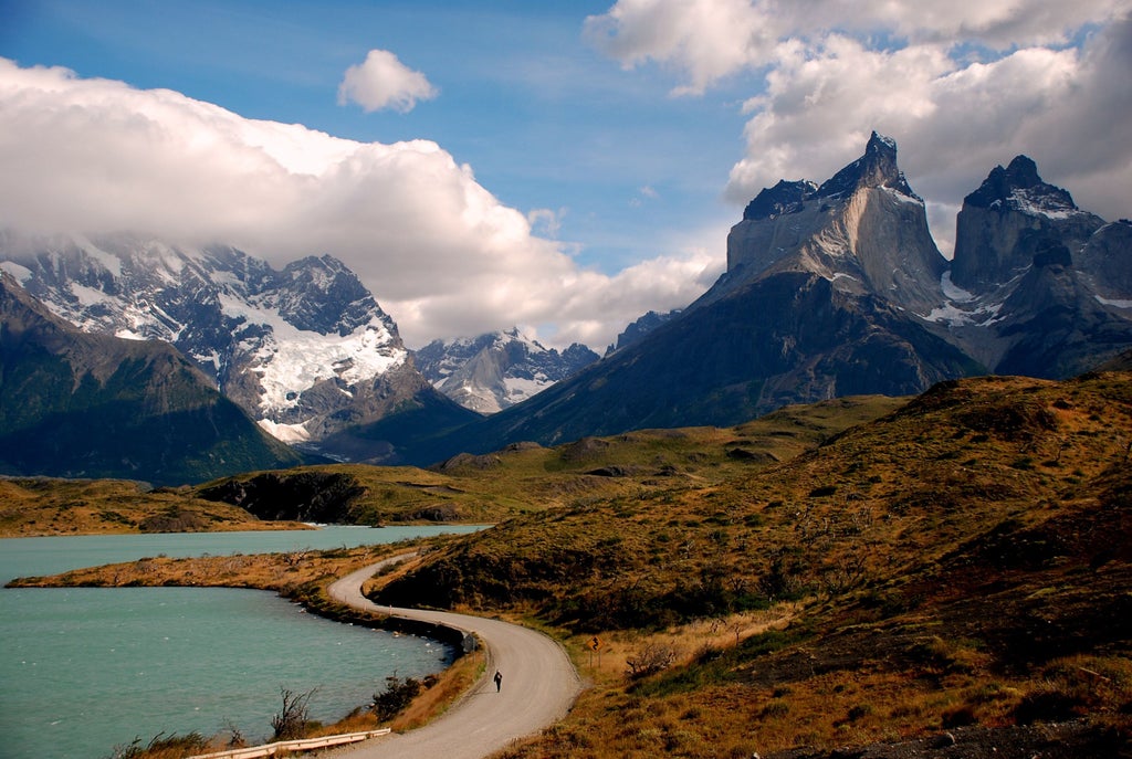 Snow-capped peaks of Torres del Paine rise behind crystal-clear turquoise lake, with wispy clouds reflecting in pristine mountain waters