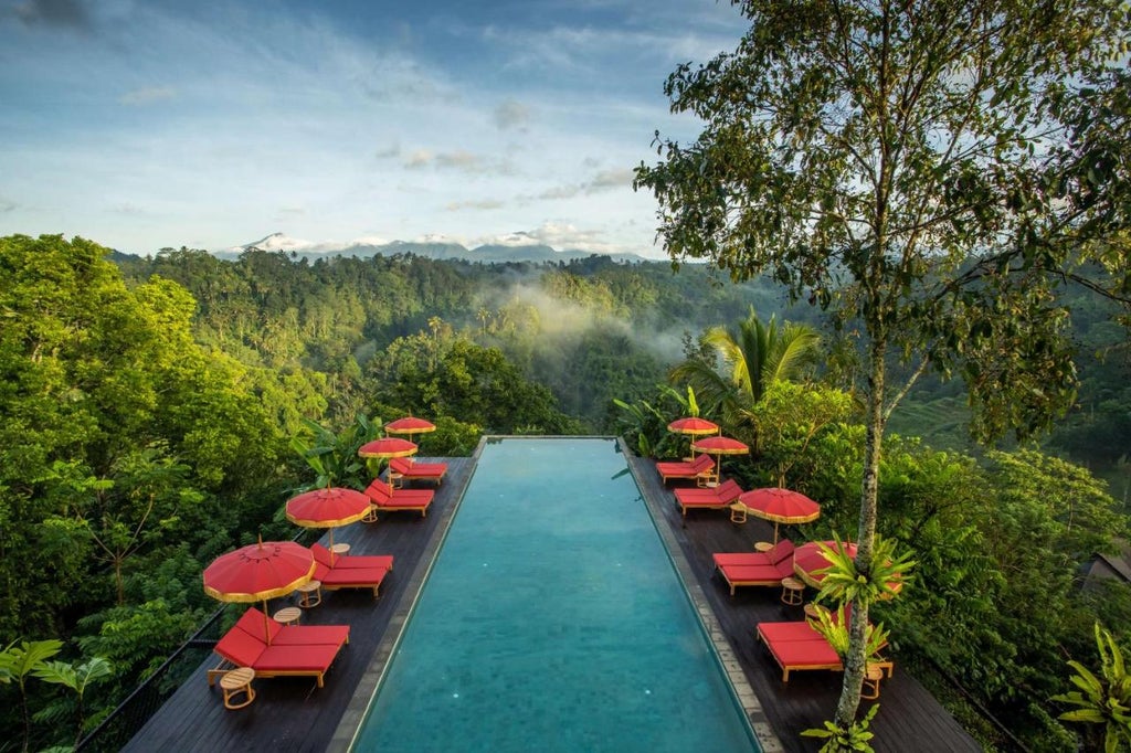 Infinity pool overlooking lush Balinese jungle valley, wooden deck with lounge chairs, luxury open-air villa architecture at sunset