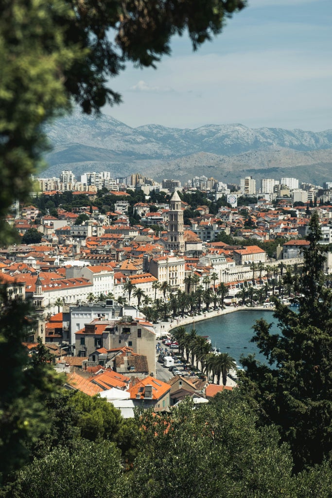 Tour guide leads visitors through charming cobblestone streets of coastal Croatia, passing medieval stone buildings and red-tiled roofs