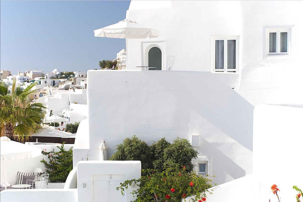 Luxurious white cliffside hotel in Santorini with infinity pools cascading down levels, overlooking the deep blue Aegean Sea