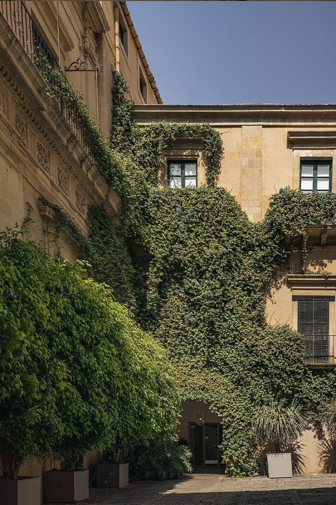 Historic Sicilian palazzo with elegant balconies, warm terracotta facade, and lush Mediterranean garden overlooking scenic coastal landscape in Noto