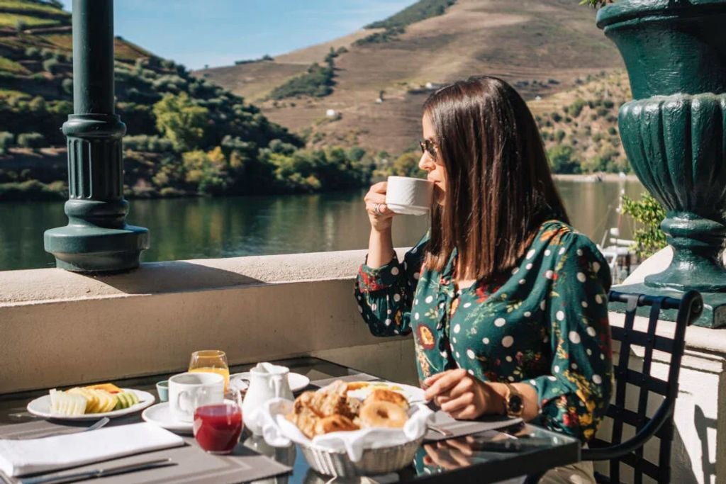 Luxurious stone hotel with terraced vineyards in Douro Valley, featuring elegant balconies and traditional Portuguese architecture at sunset