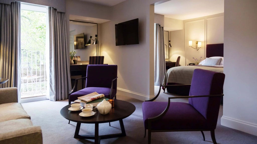 Luxurious junior suite with elegant wooden furnishings, soft neutral tones, plush king bed, and large windows overlooking historic British architecture.