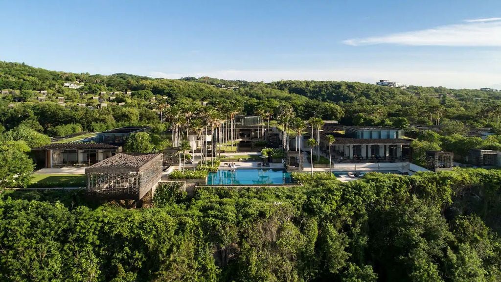 Luxurious infinity pool extending over clifftop with panoramic ocean views, modern wooden cabanas and sleek resort architecture at sunset