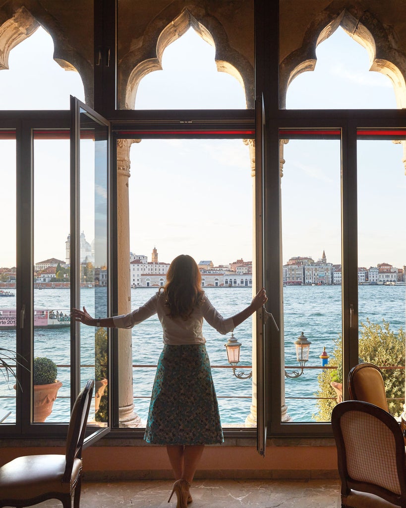 Elegant Venetian hotel with terracotta walls and arched windows overlooking a serene pool surrounded by manicured gardens and palm trees