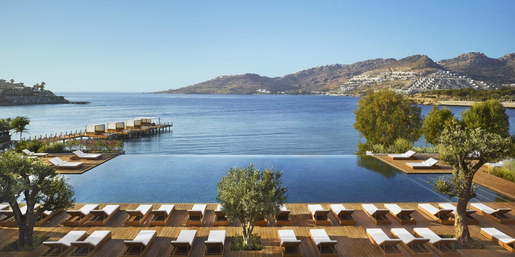 White modernist luxury resort with infinity pool overlooking Aegean Sea, nestled among pine trees on Bodrum's hillside at sunset