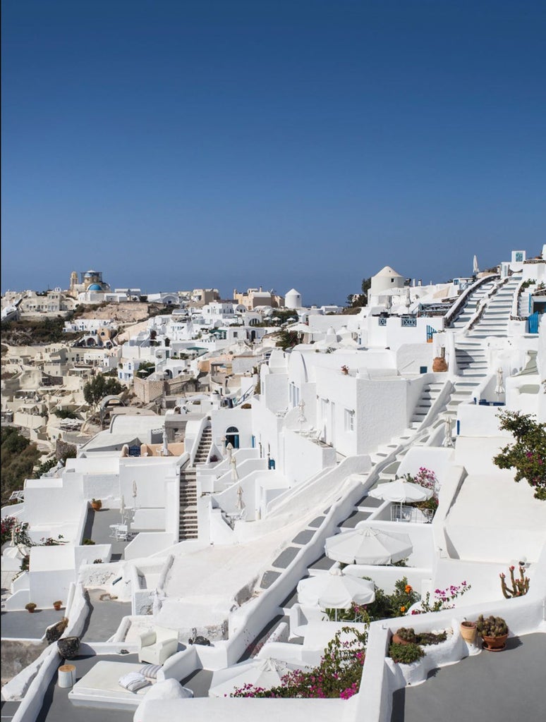 Luxurious white-washed hotel built into Santorini's cliffs, featuring infinity pools and terraces overlooking the deep blue Aegean Sea