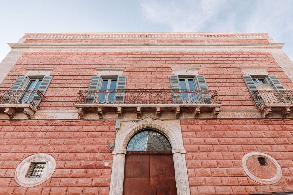 Luxurious pink baroque hotel facade with ornate balconies and elegant architectural details in historic Italian urban setting at golden hour