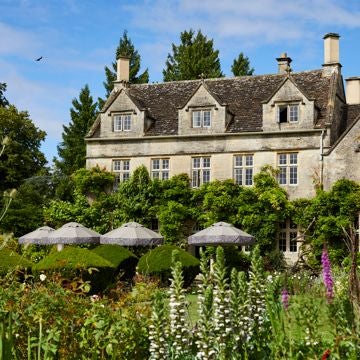 Rustic luxury hotel nestled in Devon countryside, stone facade with lush gardens, elegant exterior highlighting traditional British countryside charm