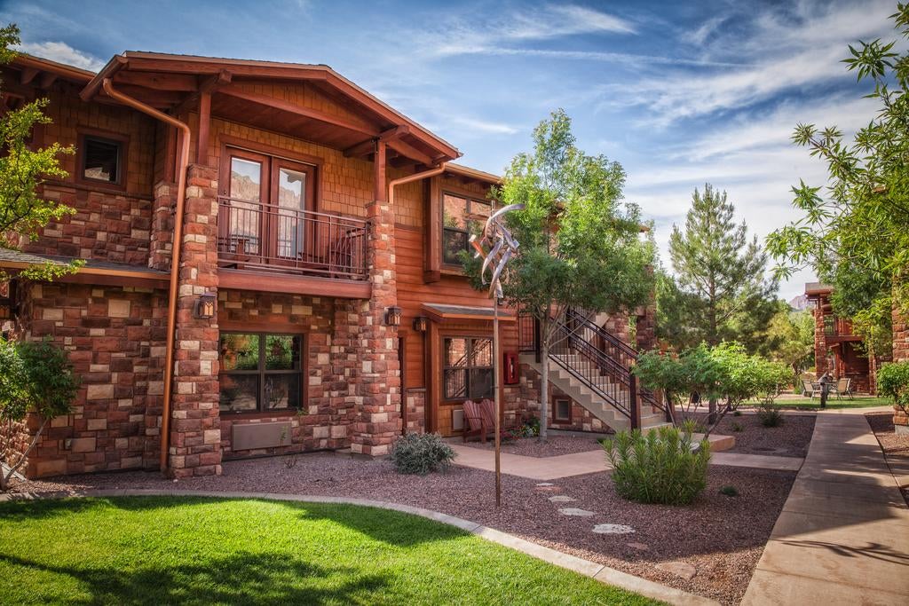 Luxurious mountain lodge with rustic stone and wood facade nestled against red cliffs, featuring modern balconies and landscaped grounds